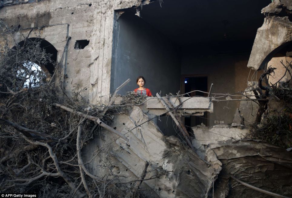 A young girl stands in her damaged home in Gaza following an air strike.