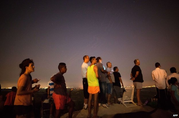 Israelis watching the bombardment of Gaza from near Sderot on Saturday evening Palestinians pass a damaged house after a Palestinian rocket hit Hebron in the West Bank, 12 July. Credit: AFP