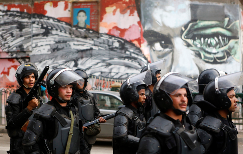 riot police walk in frong of graffiti depicting Bassem Mohsen along Mohamed Mahmoud during the third anniversary of the Mohamed Mahmoud Clashes. Credit: Reuters