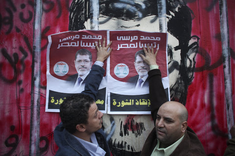 In this picture, we can see two individuals attempting to conceal the anti-MB artwork in the background by pasting posters of Morsi. (Photo credit: Tara Todras-Whitehill for The New York Times)