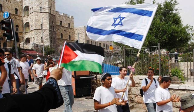 Woman waves Palestinian flag as Israeli youths with Israeli flag walk by in Jerusalem. Credit:  Reuters