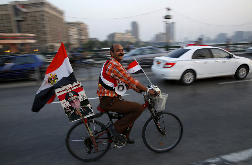 A supporter of Egyptian President Abdel-Fattah El-Sisi carries his poster on his bike as he celebrates with others for Thursday's opening of the new Suez Canal, riding on the Qasr El Nile Bridge in Cairo, Egypt, Wednesday, Aug. 5, 2015 (AP)