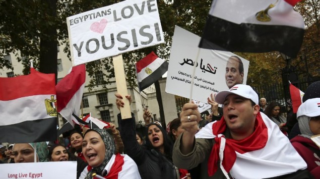 A supporter (C) welcoming the expected visit of Egyptian President Abdel Fattah el-Sissi holds a placard as other supporters wave Egyptian flags outside Downing Street in central London on November 5, 2015. (AFP PHOTO / JUSTIN TALLIS)
