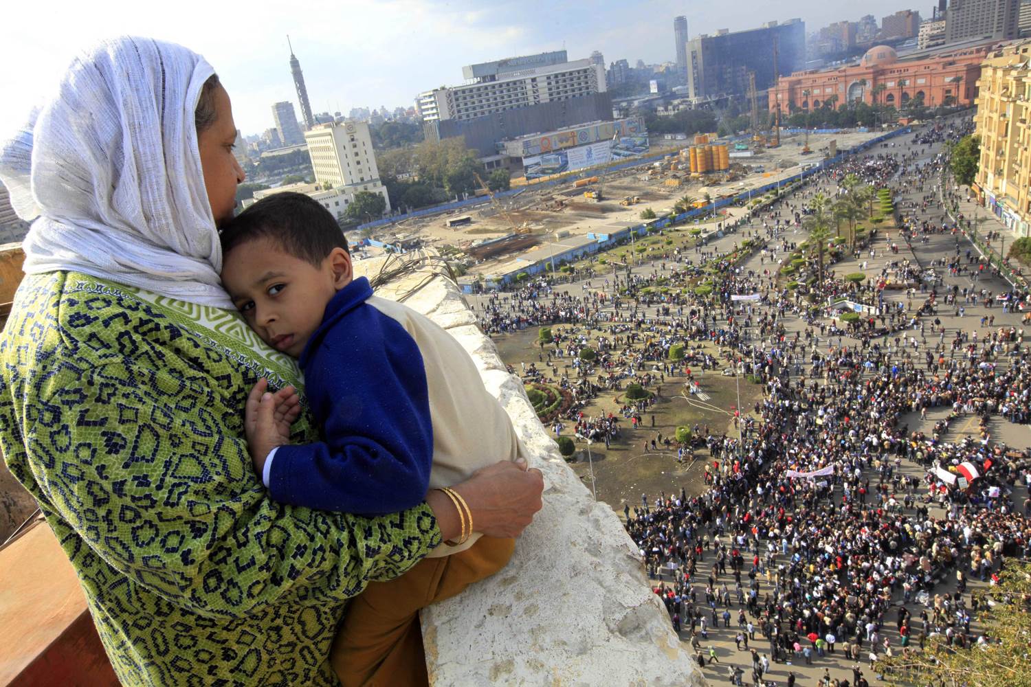 An Egyptian mother watched as thousands of Egyptian protesters gathered at Tahrir Square in Cairo in January 2011. The ruling National Democratic Party building can be seen burned at top right behind the Egypt museum. Photo: Amr Nabil, AP