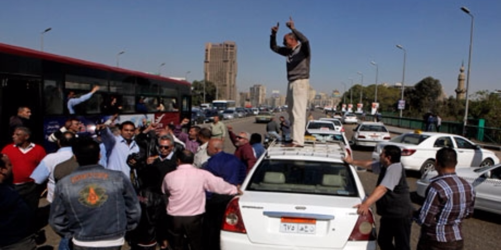 An Egyptian taxi driver stands on his car as he and others block part of the 6th October bridge in central Cairo, Egypt, 2013. Photo: AP 