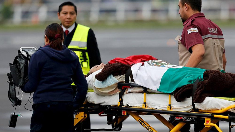 Paramedics wheel a Mexican tourist covered with a Mexican flag, who was injured during an attack in Egypt, toward a helicopter after their arrival to the presidential hangar in Mexico City, September 18, 2015. REUTERS/Tomas Bravo