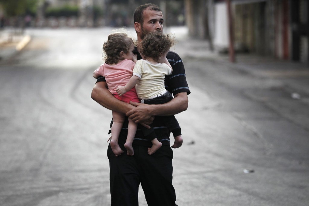 A Palestinian man carrying children flees the Shujayeh neighbourhood. REUTERS/Finbarr O'Reilly